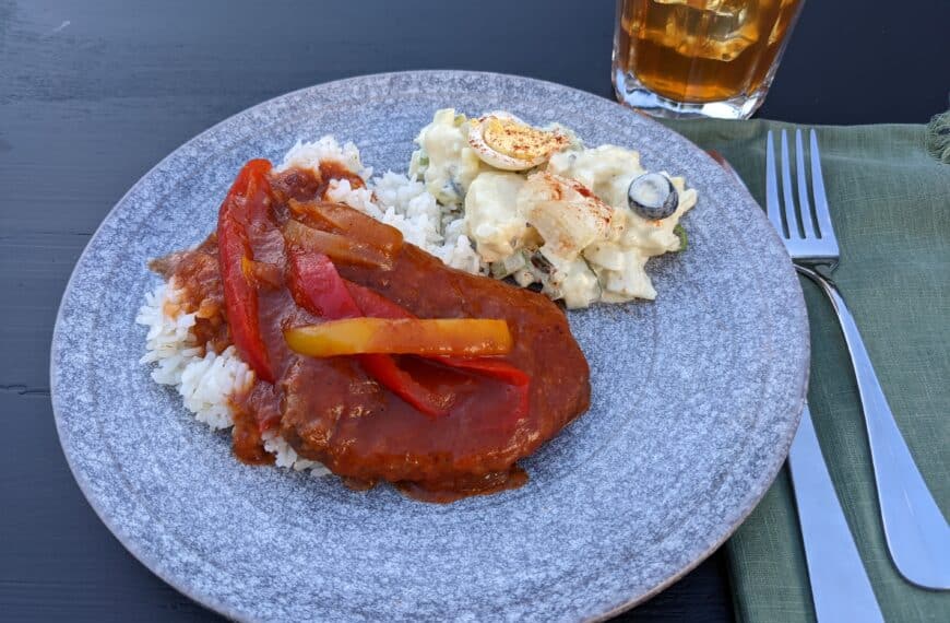 Country style cube steak on a grey plate with potato salad, in the background is a glass of iced tea, a knife and fork