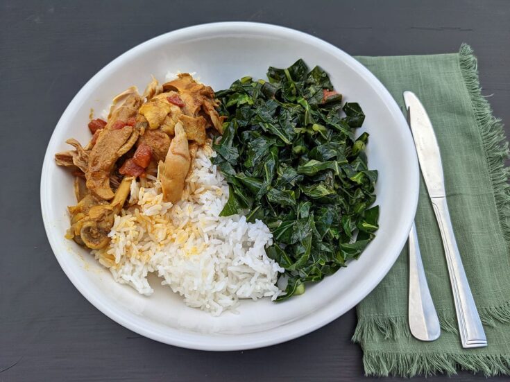 Stewed chicken over rice to the left of collard greens in a white bowl on a black background