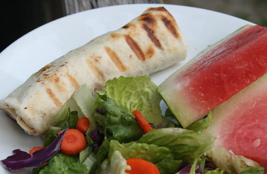 Grilled Chicken Burrito on a plate with a green salad and sliced watermelon