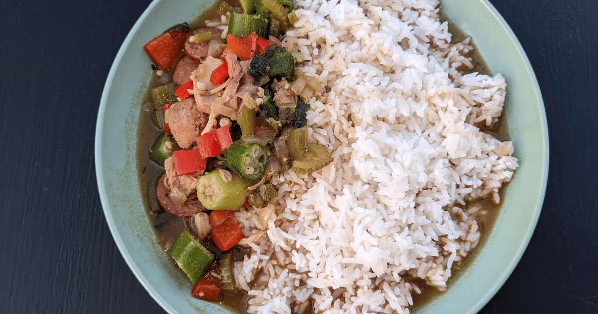 chicken gumbo and white rice in a pale green bowl on a black background