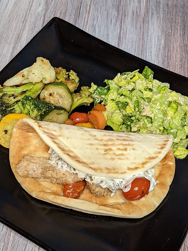 Schwarma-inspired chicken on pita bread with a side of vegetables and caesar salad.