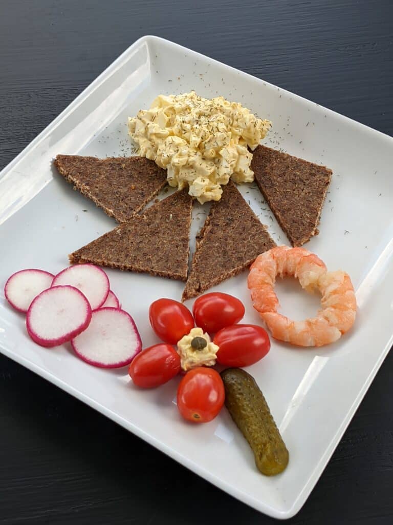 Egg salad with russian bread, sliced radishes, grape tomatoes arranged in a flower with pickle stem and two cooked shrimp